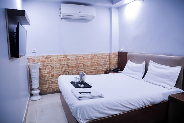 A hotel room with a bed, a nightstand, a wall-mounted TV, an air conditioner, and a brick-patterned accent wall.