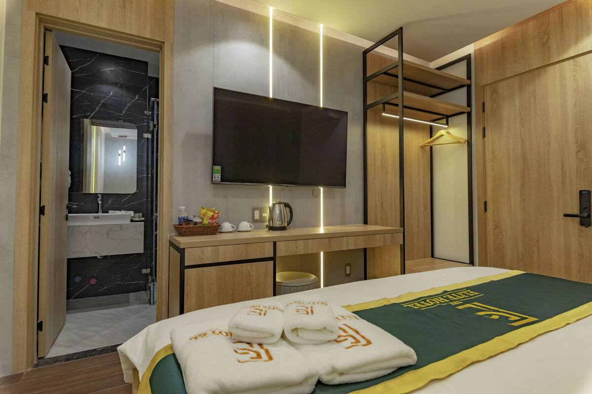 A hotel room with a bed, a TV, a desk with a mirror, a sink, and a wardrobe.