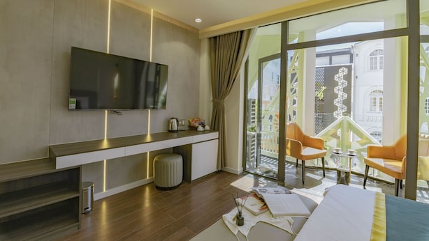 A modern hotel room with a large TV, a balcony with yellow chairs, and a view of the cityscape. - The Elite Hotel (Xuan Huong - Da Lat)