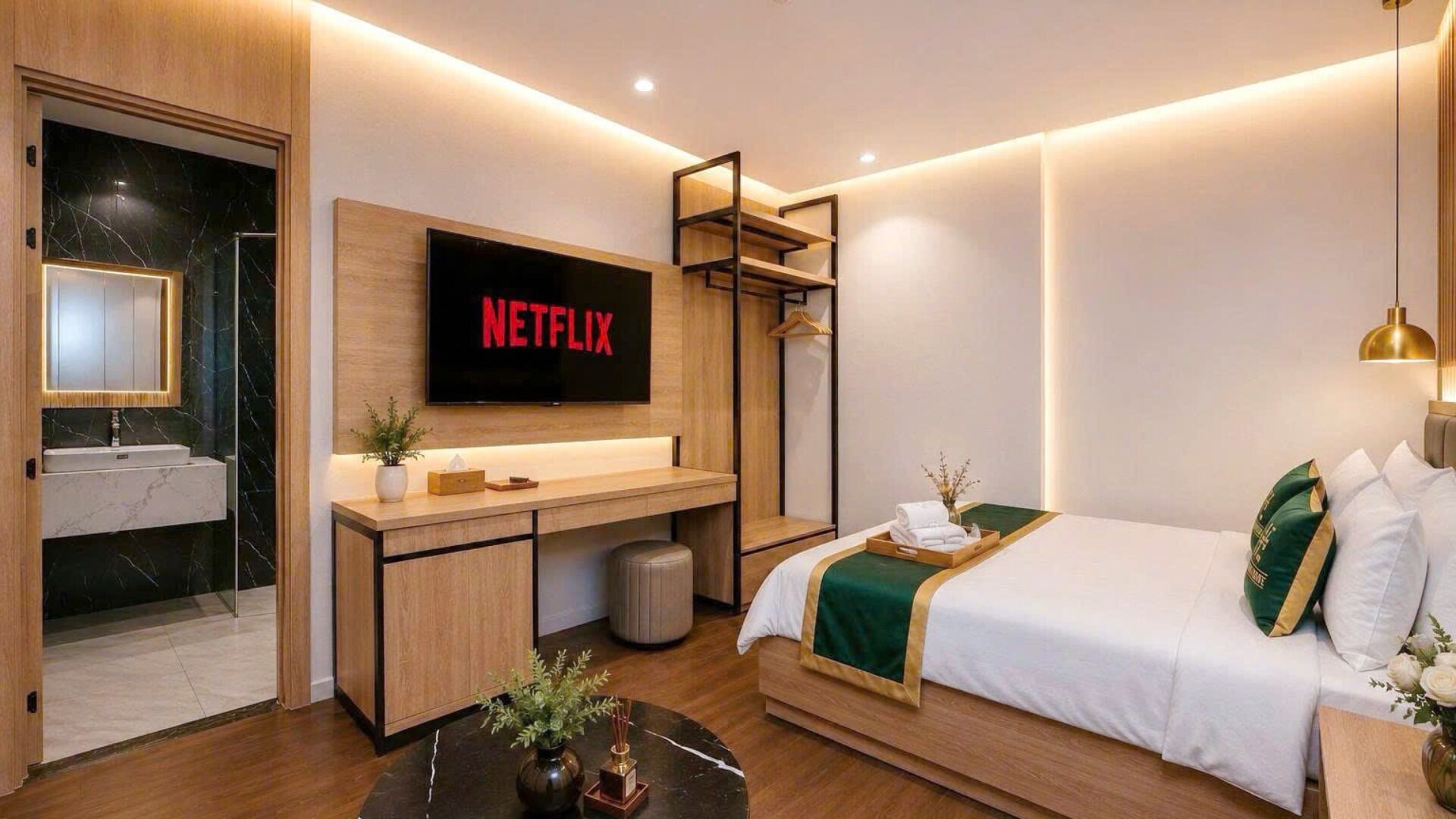 Habitación de hotel moderna con una cama, un escritorio con un televisor de pantalla plana que muestra 'NETFLIX', un baño con espejo y una planta pequeña en el escritorio.