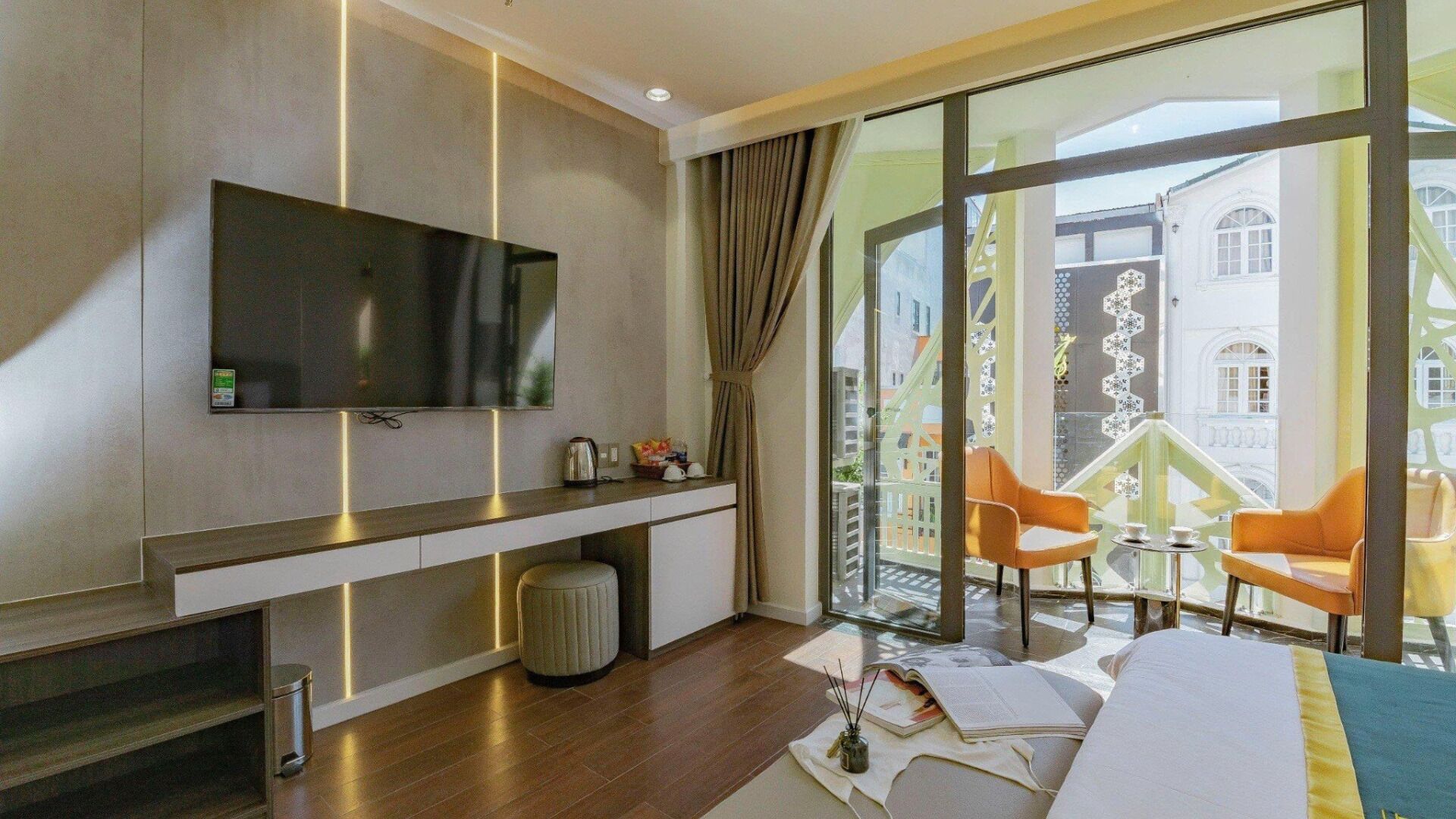 Habitación de hotel con televisor grande, sofá, una mesita y un balcón con sillas.