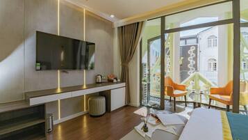 Habitación de hotel con televisor grande, sofá, una mesita y un balcón con sillas.
