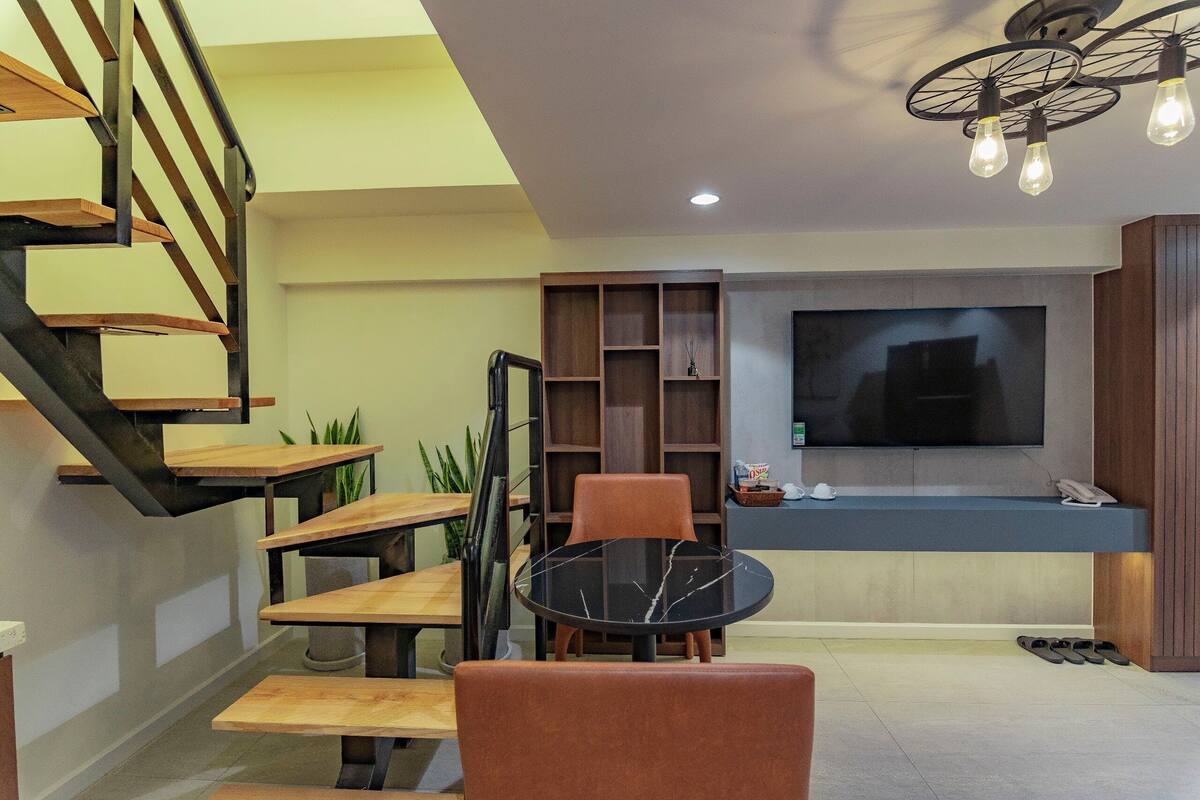 A modern living room with a staircase, a flat-screen TV, and a dining area.