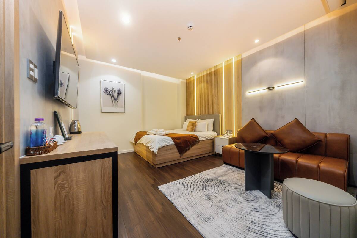 A modern hotel room with a bed, a sofa, a desk, and a small table.