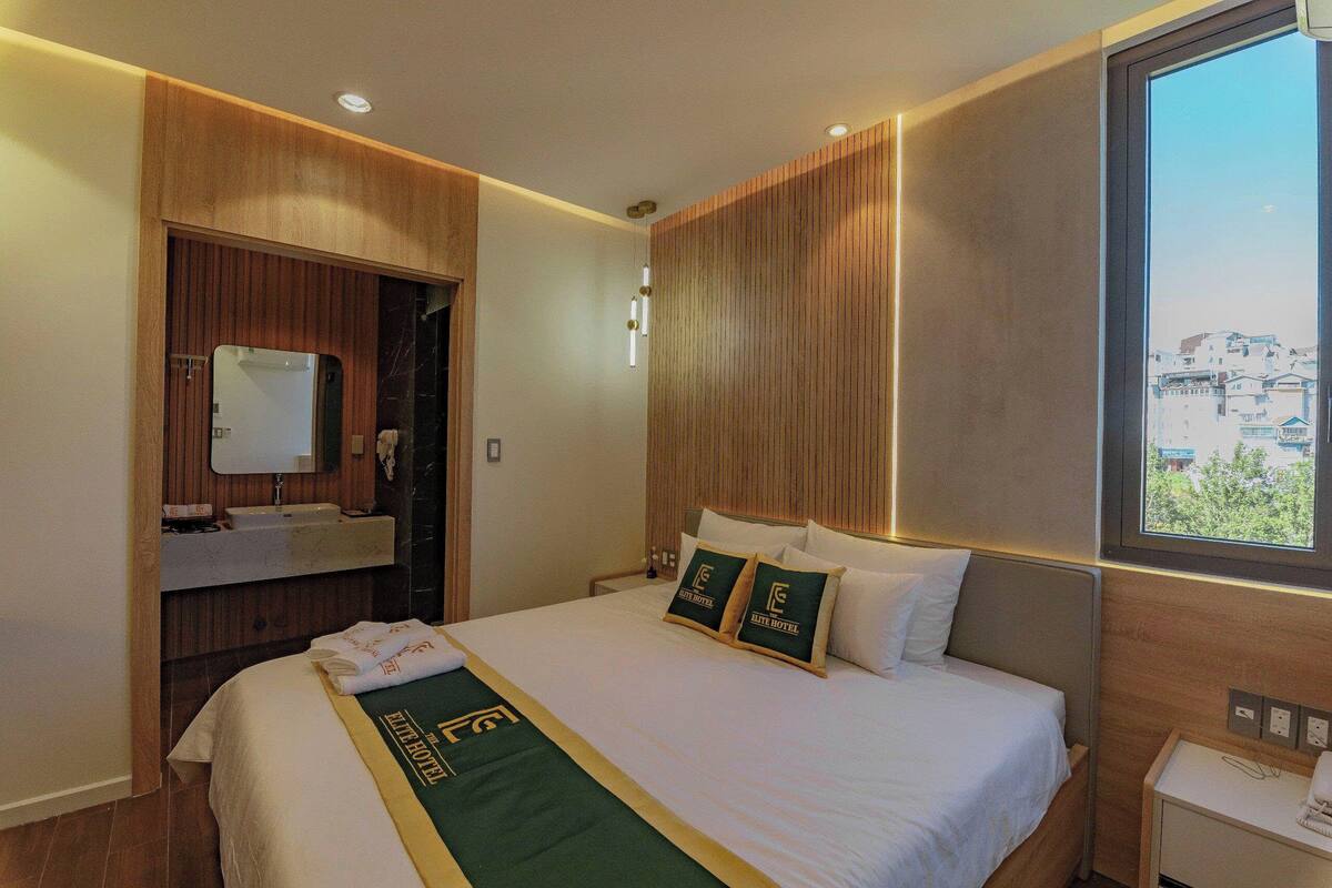 A hotel room with a bed, a vanity with a mirror, and a window with a view of buildings.