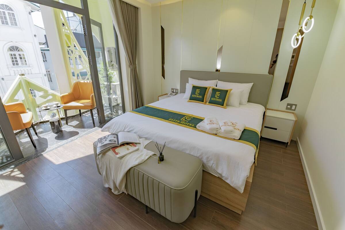 A hotel room with a large bed, a bedside table, a chair, and a view of the outside.