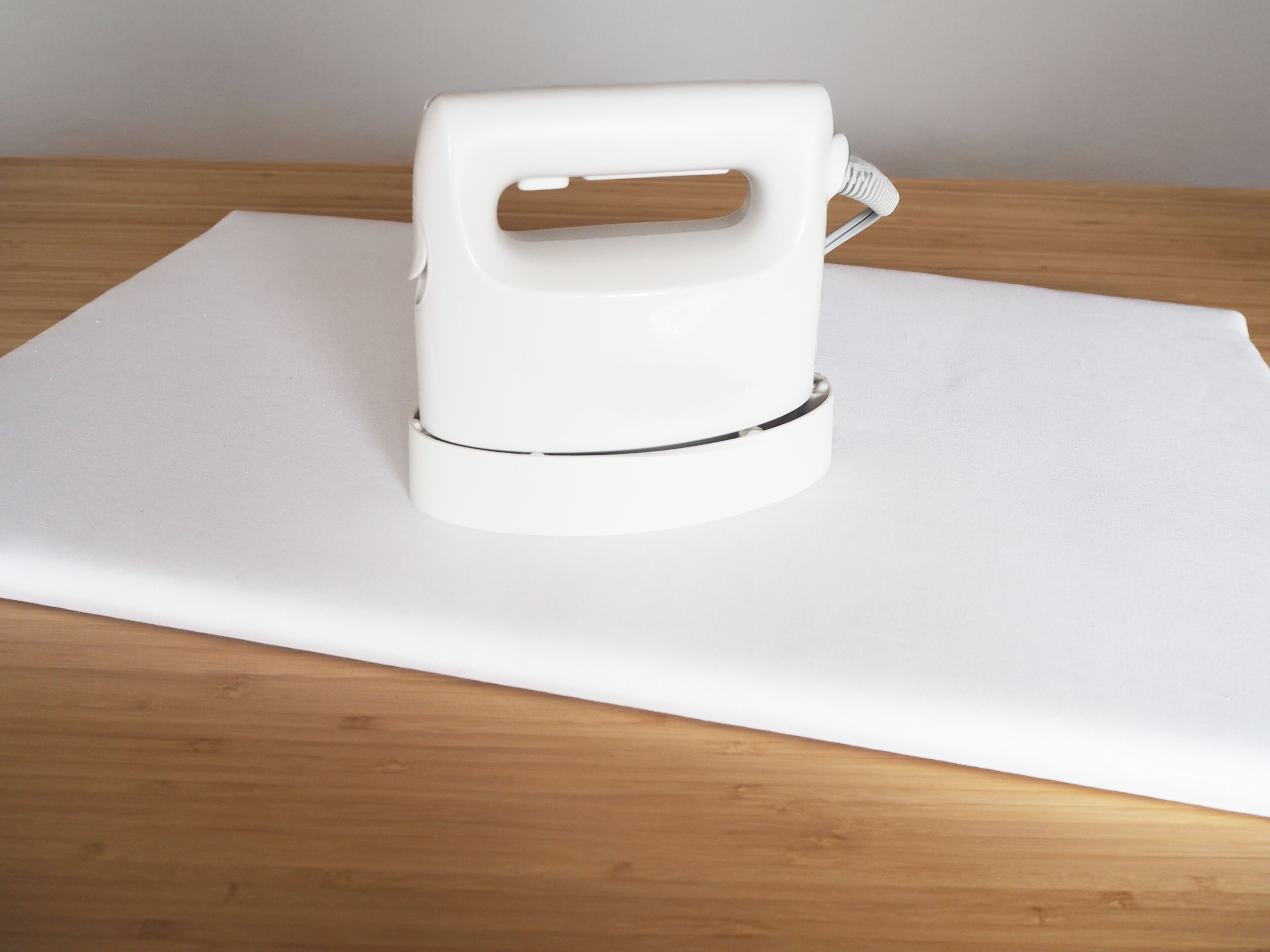 A white portable iron on a wooden table with a white cloth underneath.