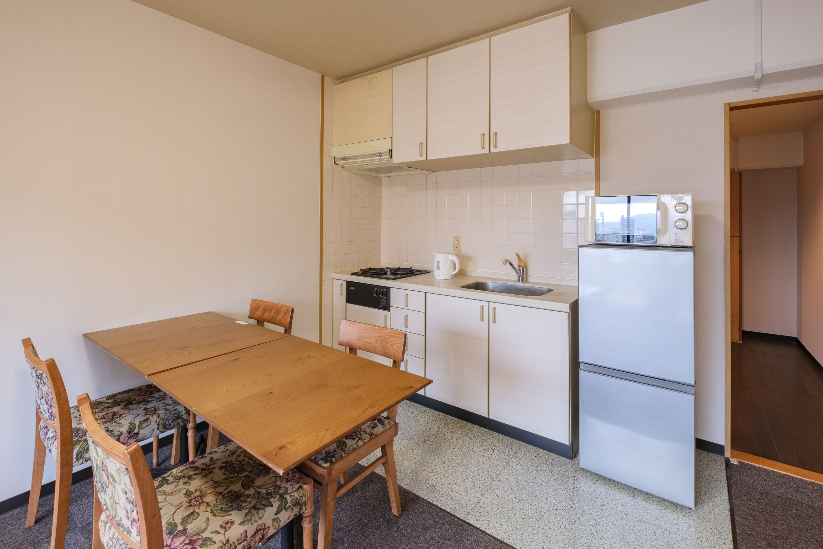 A compact kitchen with a wooden table and chairs, a microwave, a refrigerator, and a dishwasher.