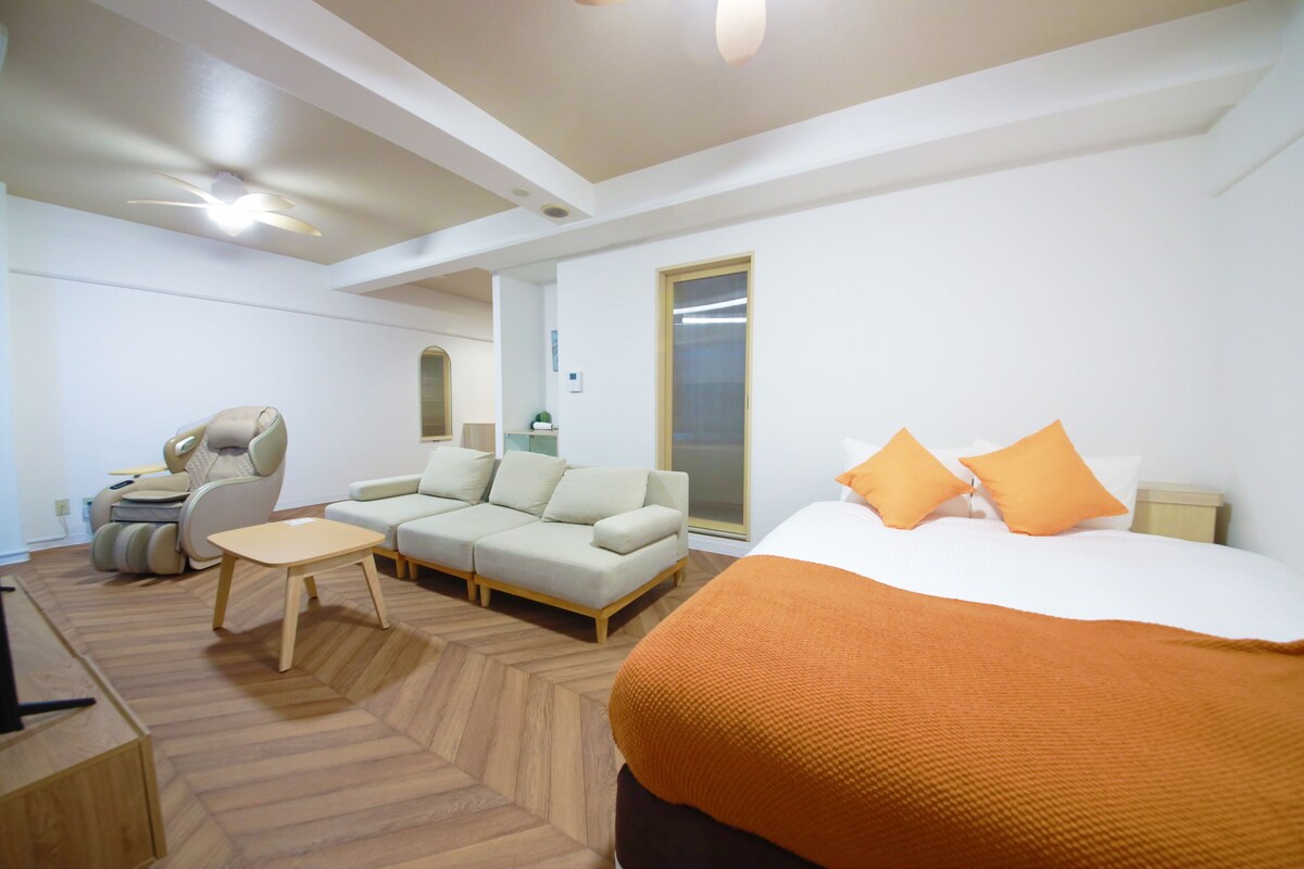Une chambre d’hôtel moderne avec un grand lit, un canapé, un fauteuil massant et une petite table.