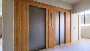 Een hal met een wand van houten panelen, een grijze lift en een deur met lichtschakelaar.