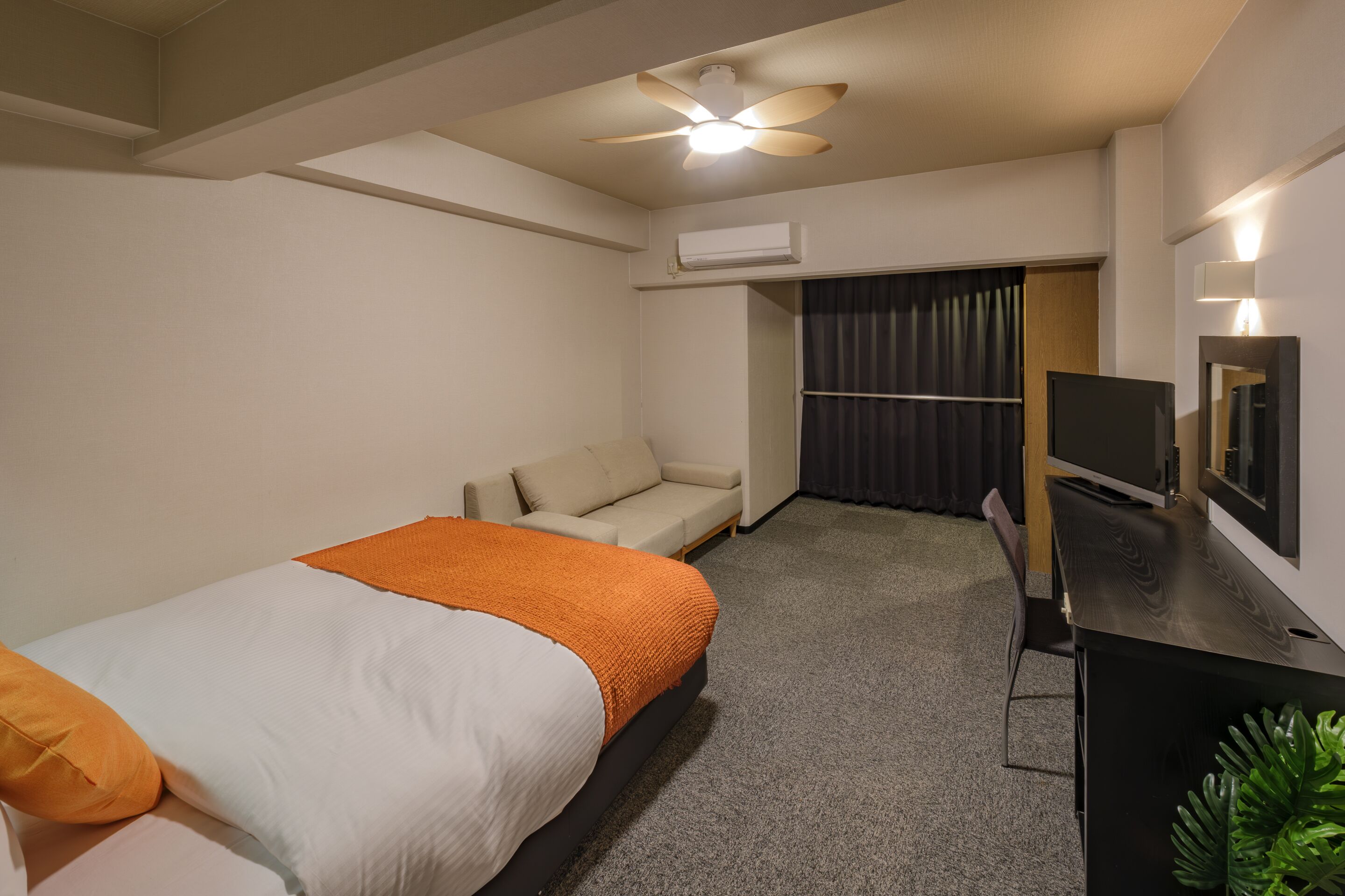 Ein Hotelzimmer mit Bett, einer Couch, einem Schreibtisch, einem Fernseher und einer Klimaanlage.