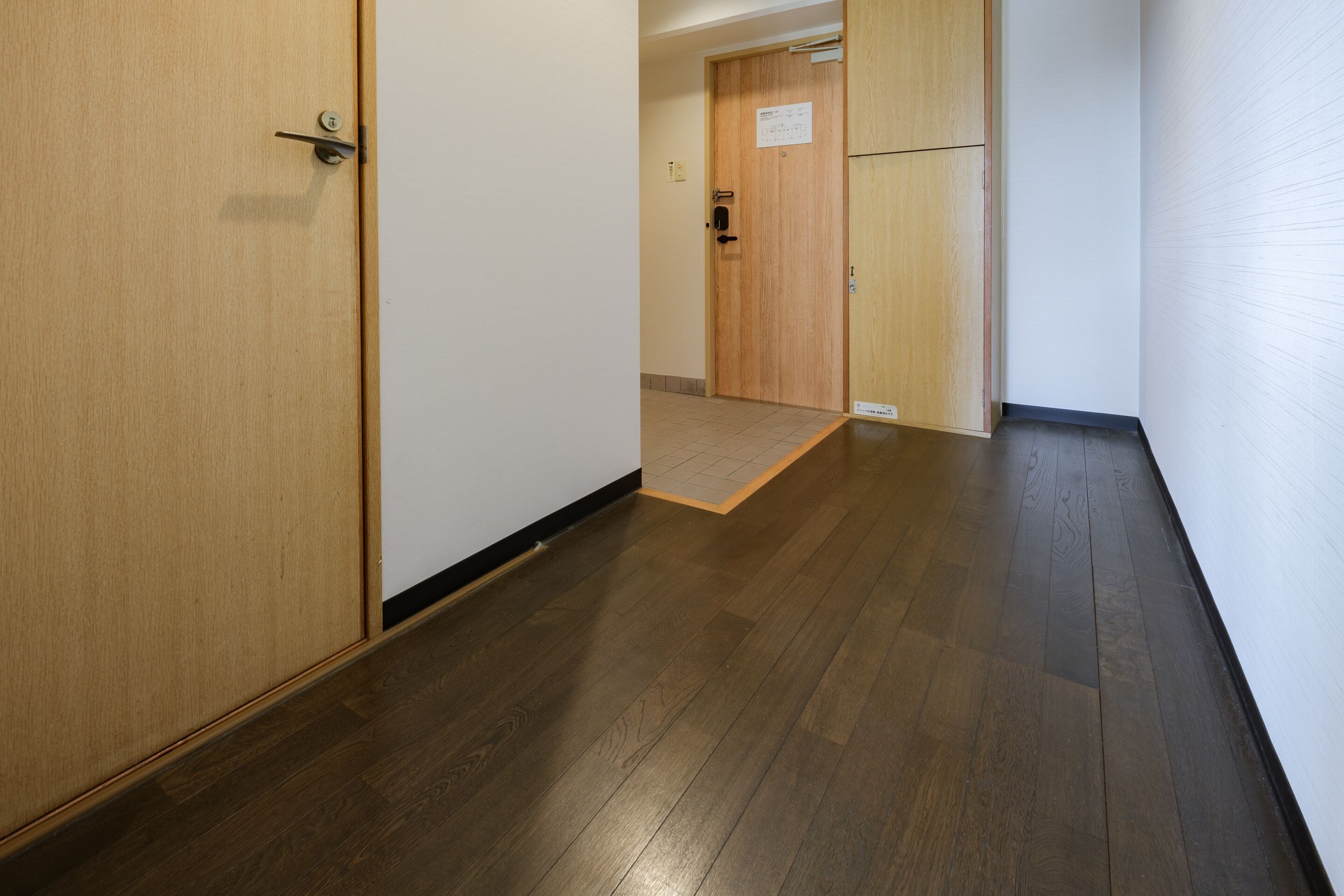 A hallway with wooden flooring, a door with a handle, and a wall with a sign.