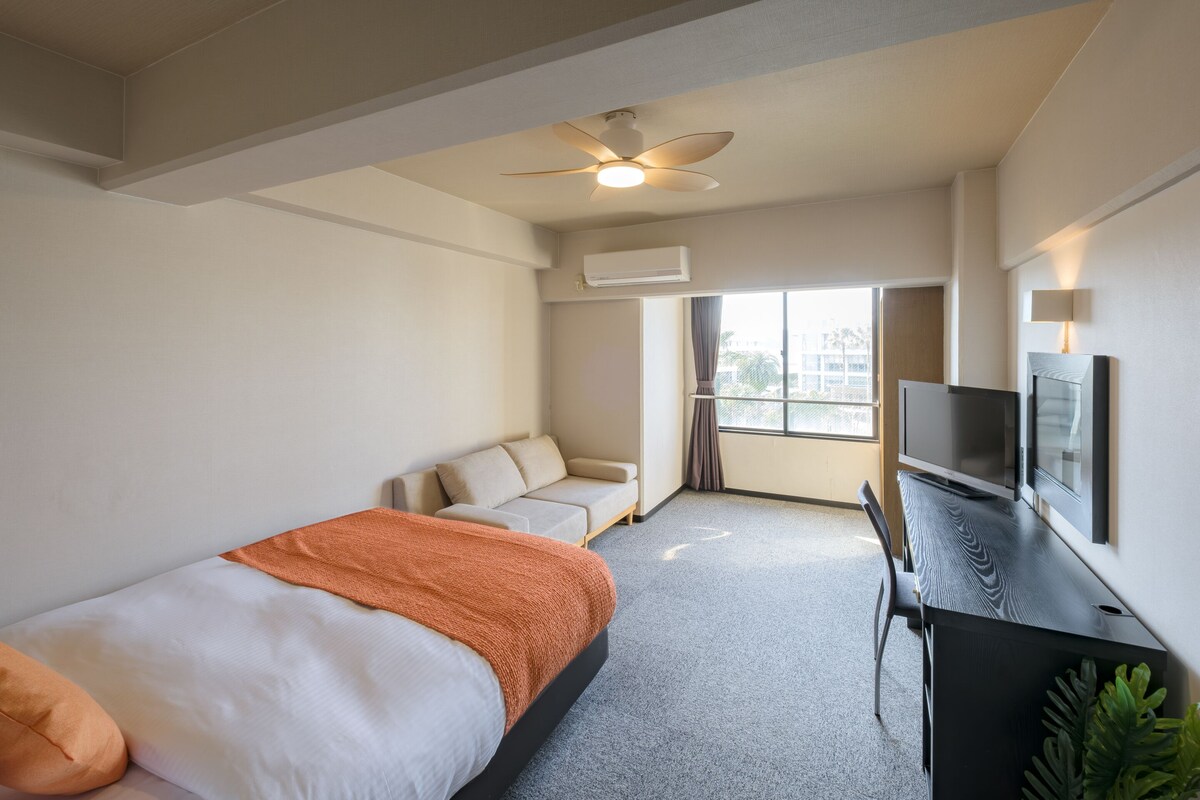 Une chambre d’hôtel avec un lit, un bureau, une télévision et une fenêtre avec des rideaux.