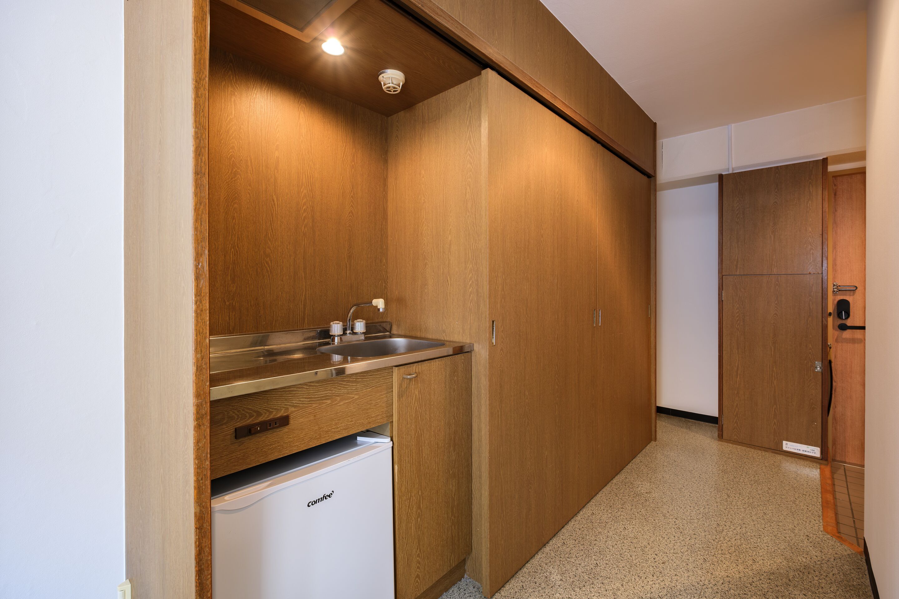 A compact kitchen with wooden cabinets, a stainless steel sink, and a built-in refrigerator.