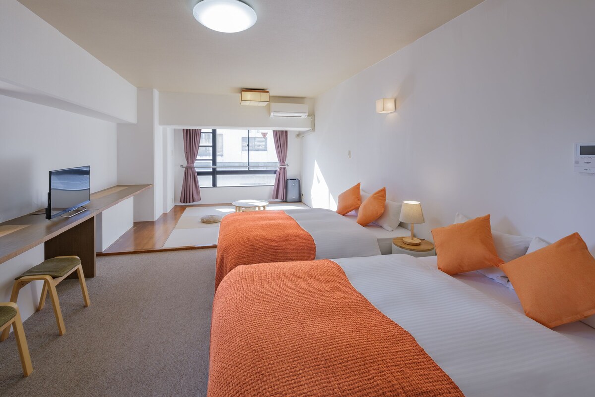 Une chambre d’hôtel avec deux lits, un bureau, une chaise et une petite table avec une lampe.