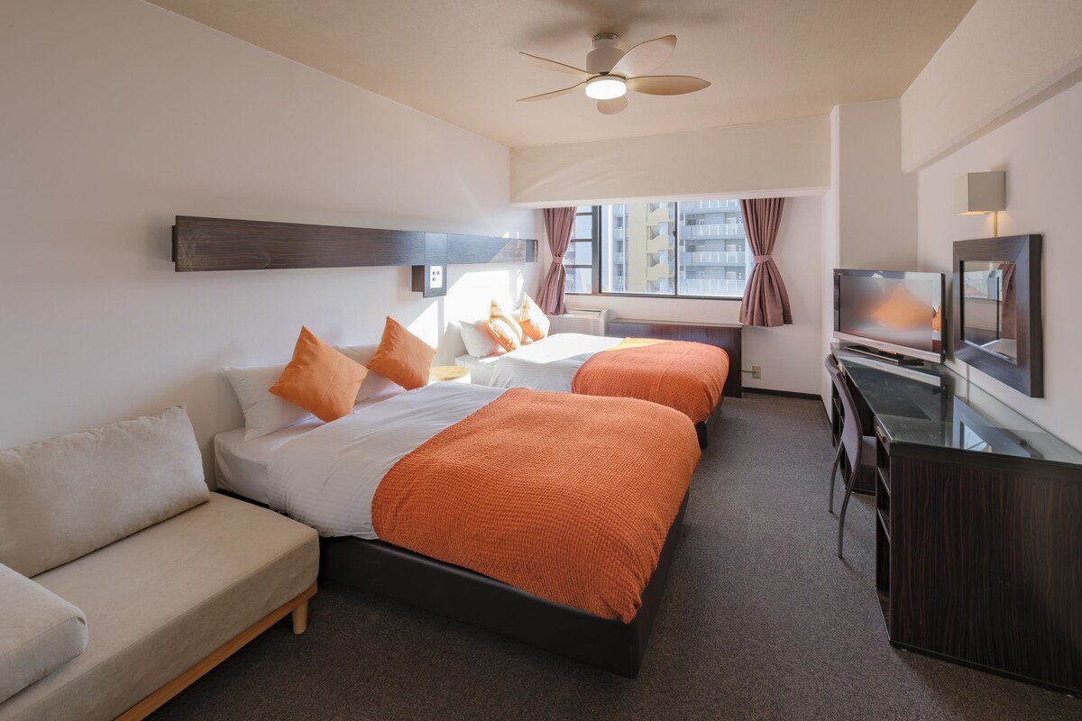 Une chambre d’hôtel avec deux lits, un canapé, un bureau et une télévision.