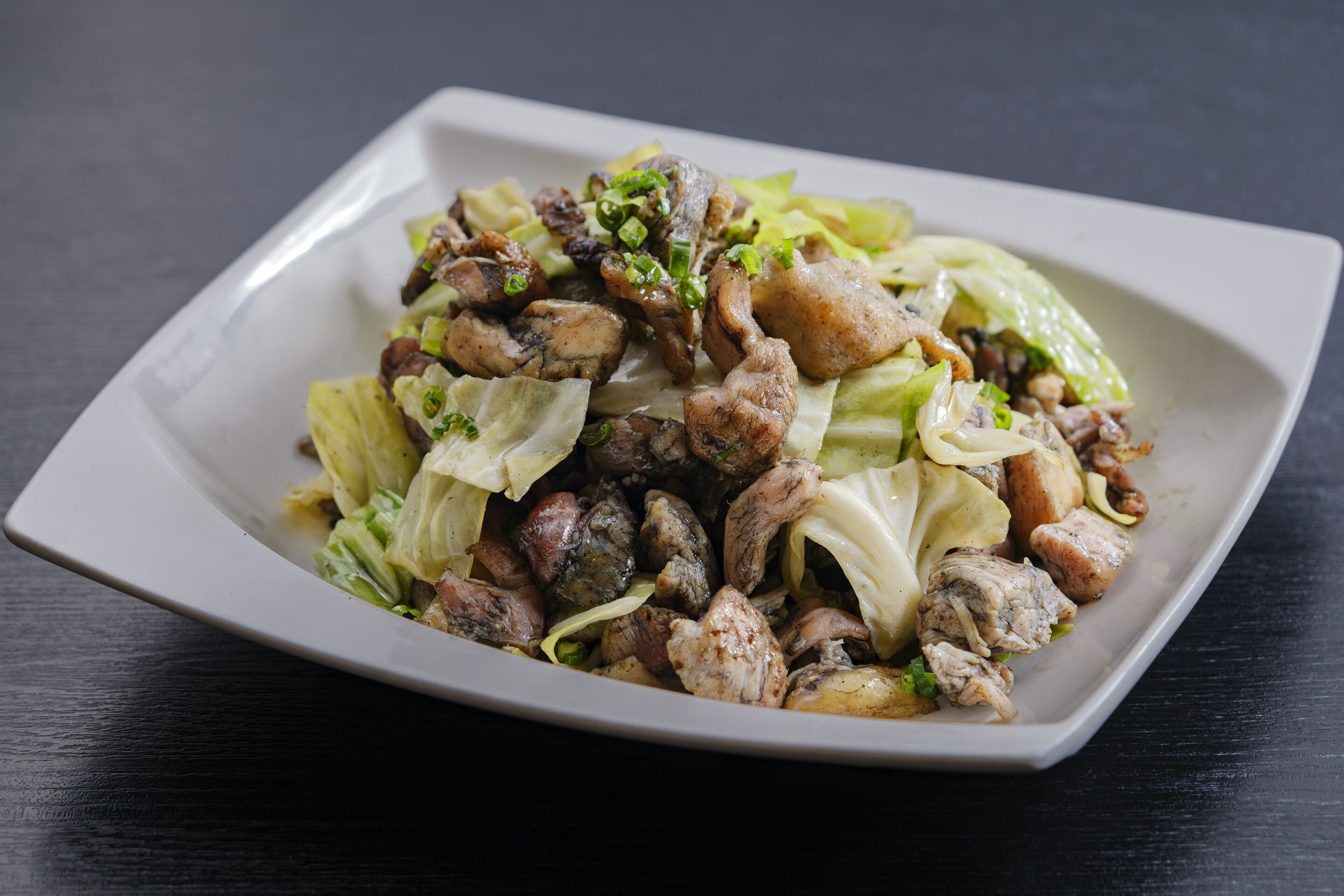 A white rectangular plate with a salad containing chicken, mushrooms, and green onions on a dark surface.