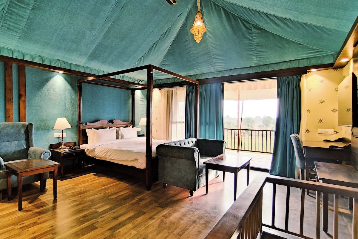 A four-poster bed with a wooden frame, a sitting chair, a desk, and a small table.