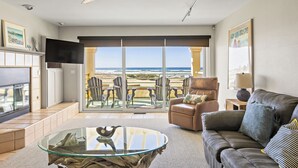 Un salon avec une table basse en verre, un canapé en cuir et un téléviseur. Il y a un balcon avec vue sur la plage.