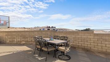 Un patio al aire libre con una mesa y sillas, un muro de ladrillo y vistas a la playa.