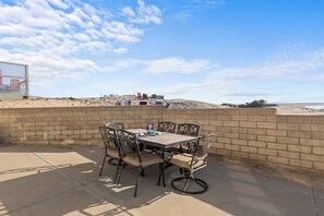 Un patio al aire libre con una mesa y sillas, un muro de ladrillo y vistas a la playa.