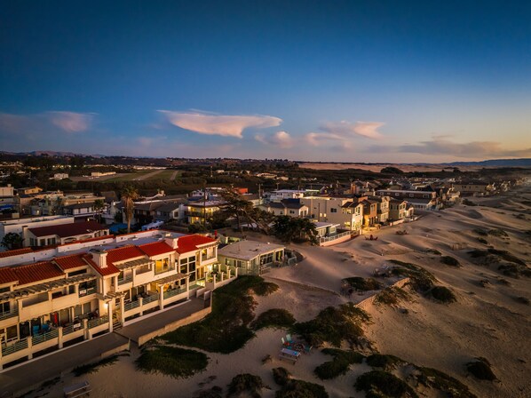 A coastal resort with multiple buildings, a sandy beach, and a clear sky. - Strandcastle Beach House - Oceanfront! - You're right on the sand! (Oceano)