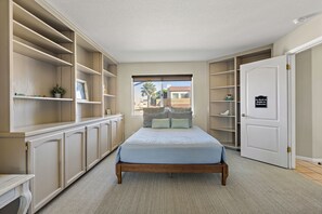 Un dormitorio con cama, estanterías empotradas, armario y una puerta con un cartel.