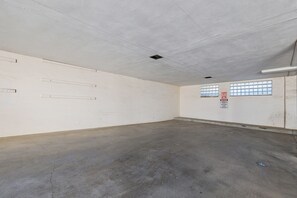 Una habitación amplia y vacía con piso de concreto y paredes blancas. Hay dos ventanas con rejas, un letrero en la pared e iluminación empotrada en el techo.