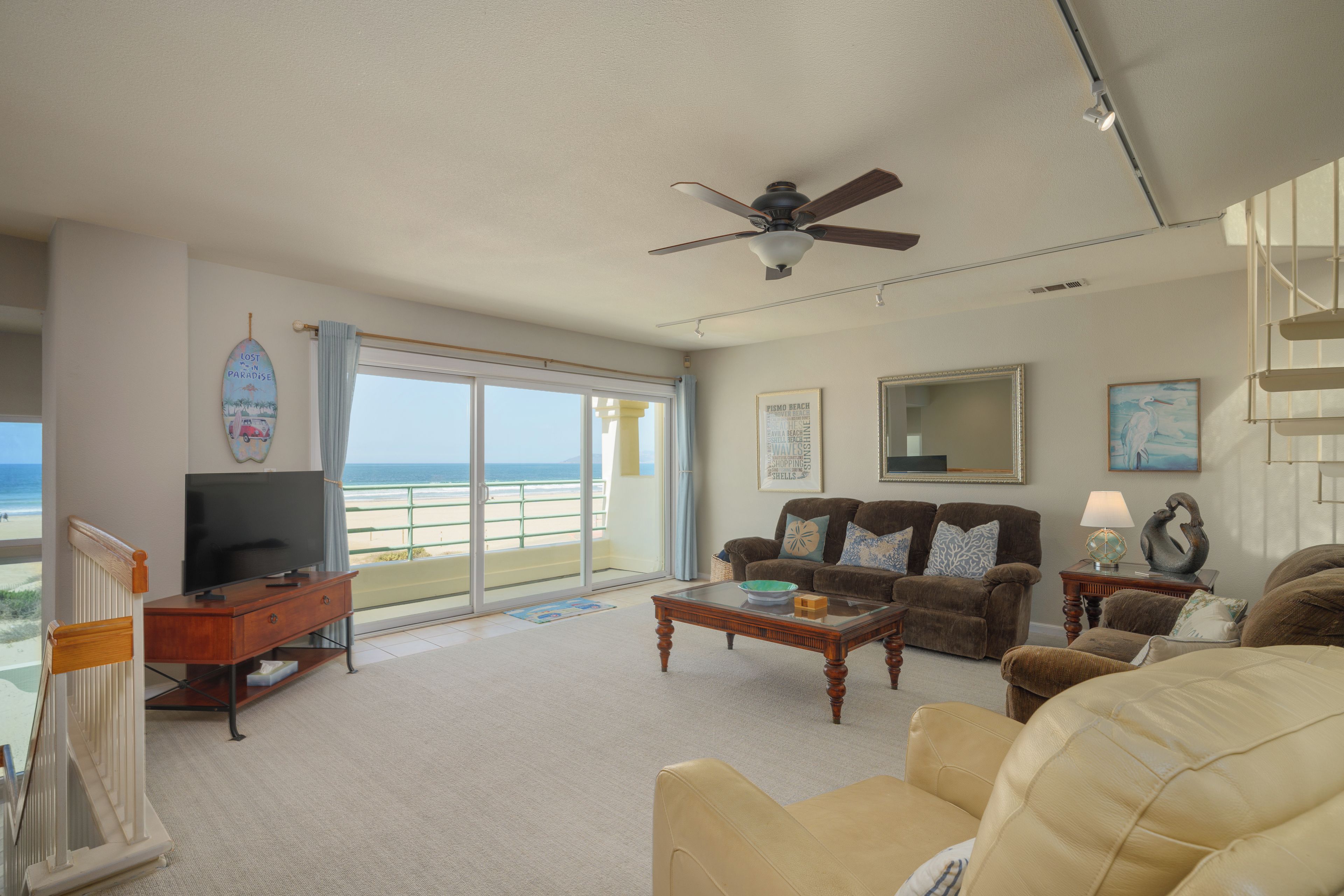 Ein geräumiges Wohnzimmer mit Fernseher, einer Sitzecke und Blick auf den Strand.