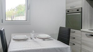 Une table à manger dressée avec des assiettes et des verres, une chaise, et une vue sur une cuisine équipée d’un réfrigérateur et d’un four.