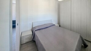 Une chambre à coucher comprenant un lit, une table de chevet, une commode et un luminaire suspendu.