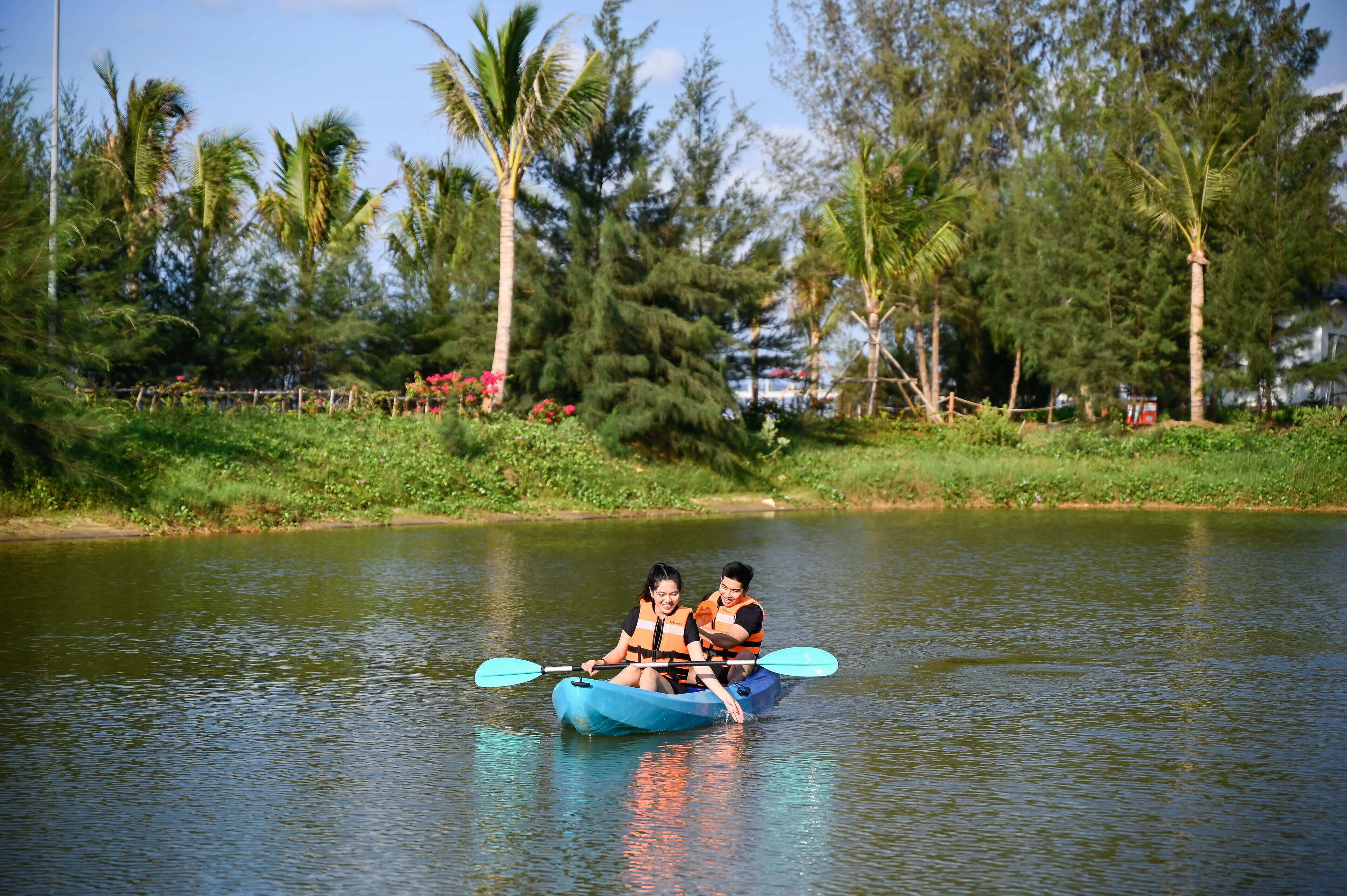 Two people in a blue kayak on a calm river surrounded by greenery and trees.
