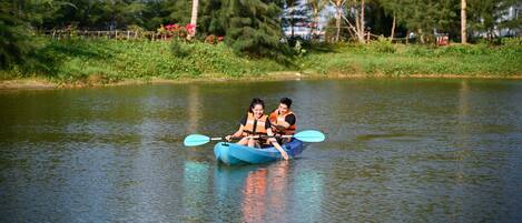 Two people in a blue kayak on a calm river surrounded by greenery and trees.