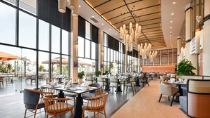 A spacious indoor dining area with high ceilings, large windows, and modern lighting fixtures. - Emerald Ho Tram Resort (Ho Chi Minh City)