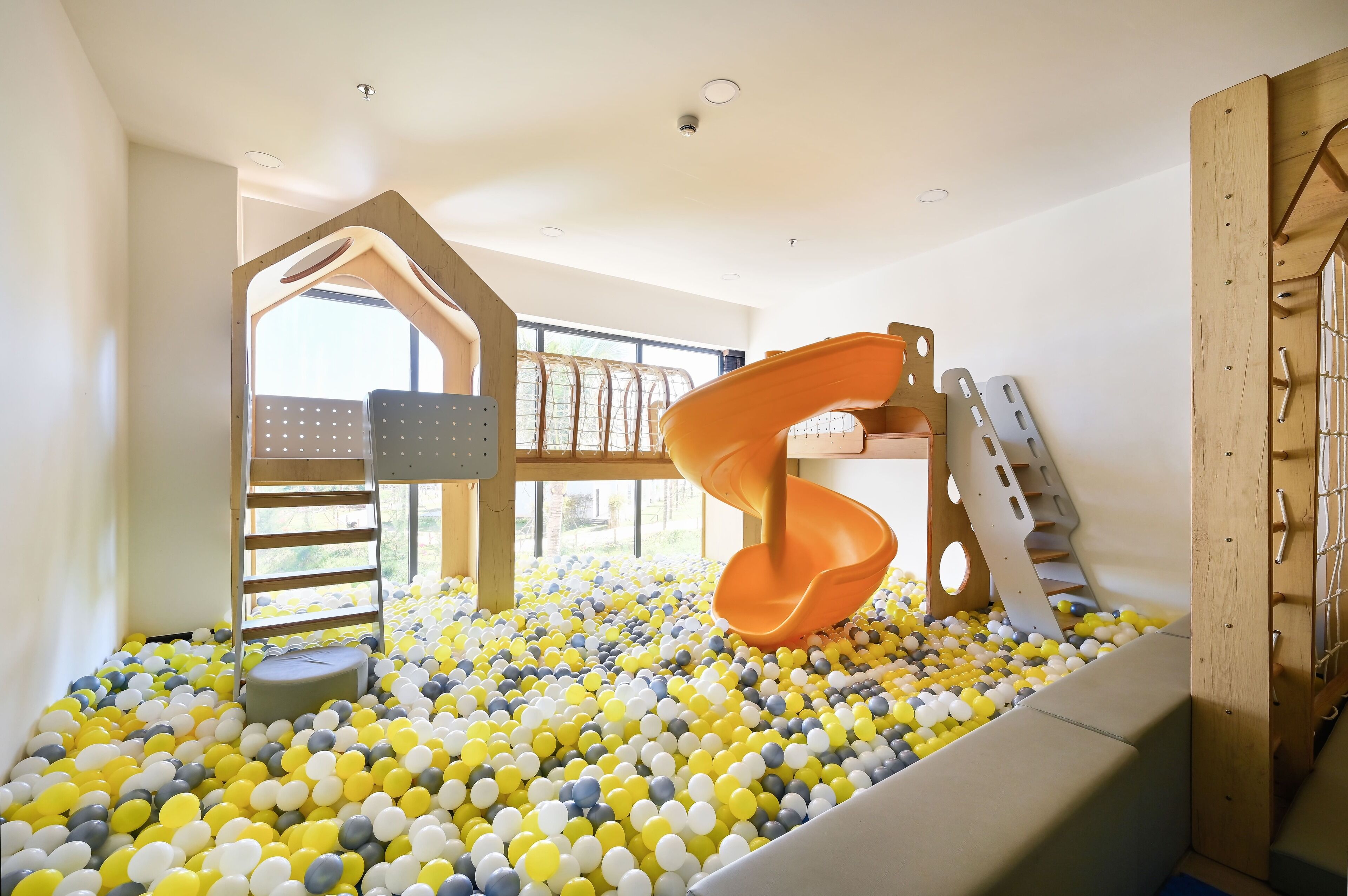 A play area with a slide, climbing structures, and a ball pit filled with yellow and white balls.