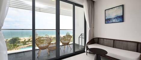 Un balcón con vistas a la playa y al océano, sillones de mimbre, un sofá y un cuadro en la pared.