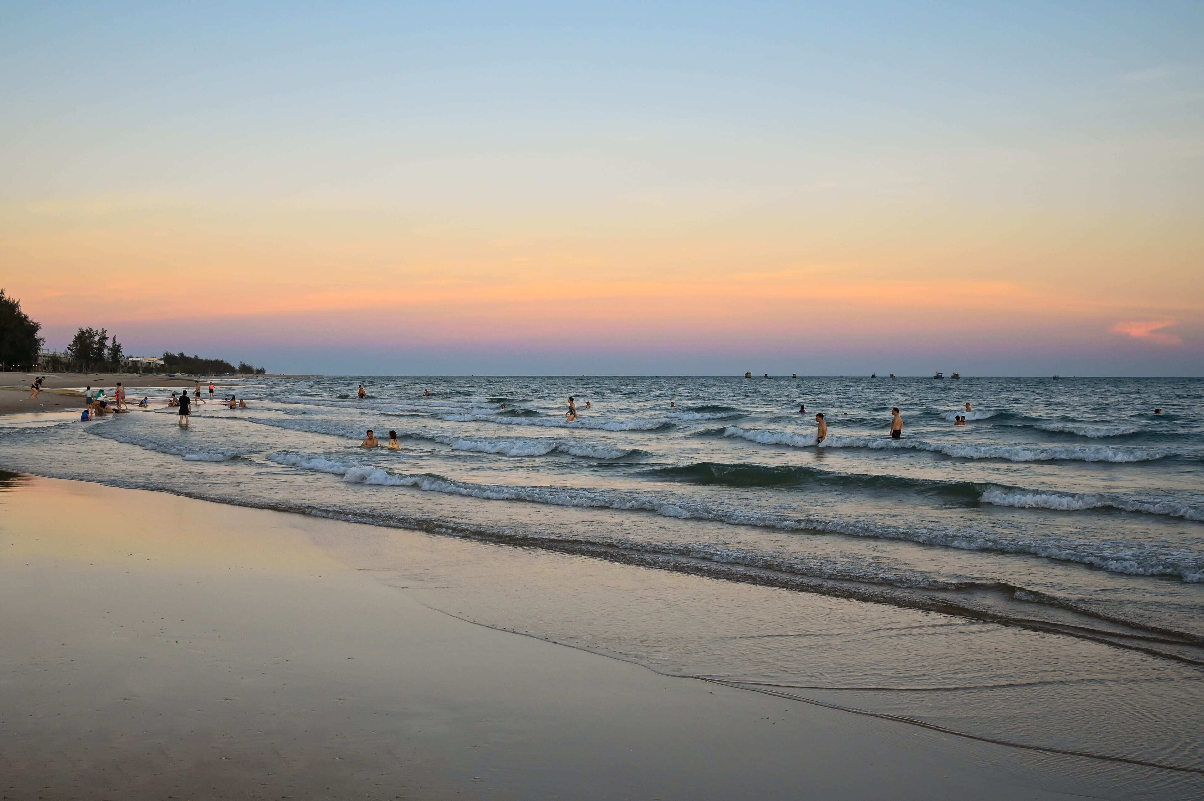Una playa con gente nadando y caminando por la orilla.