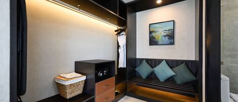 A modern hotel room with a built-in wardrobe, a seating area with cushions, a painting on the wall, and a small table with a basket.