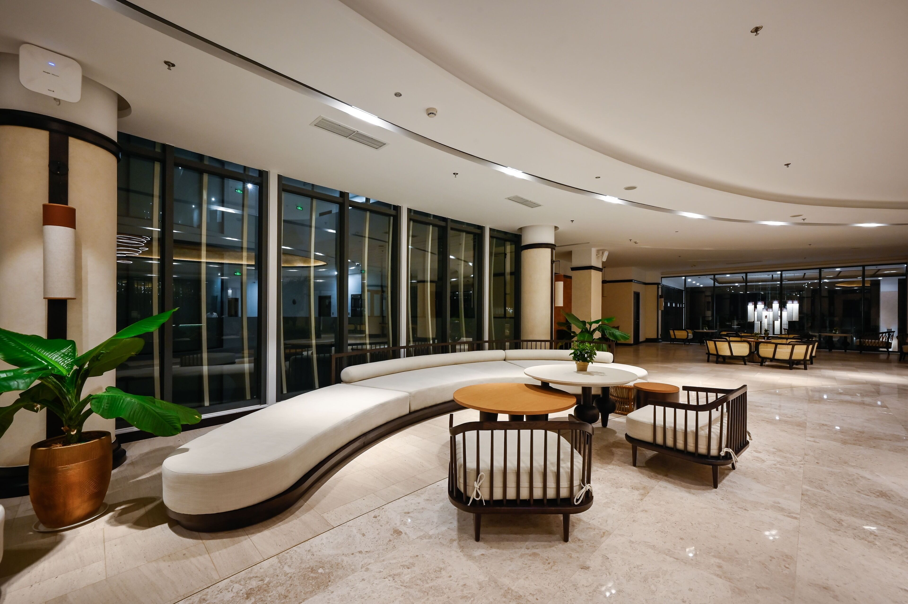 A modern lobby with a curved white sofa, a round wooden table, and two armchairs.