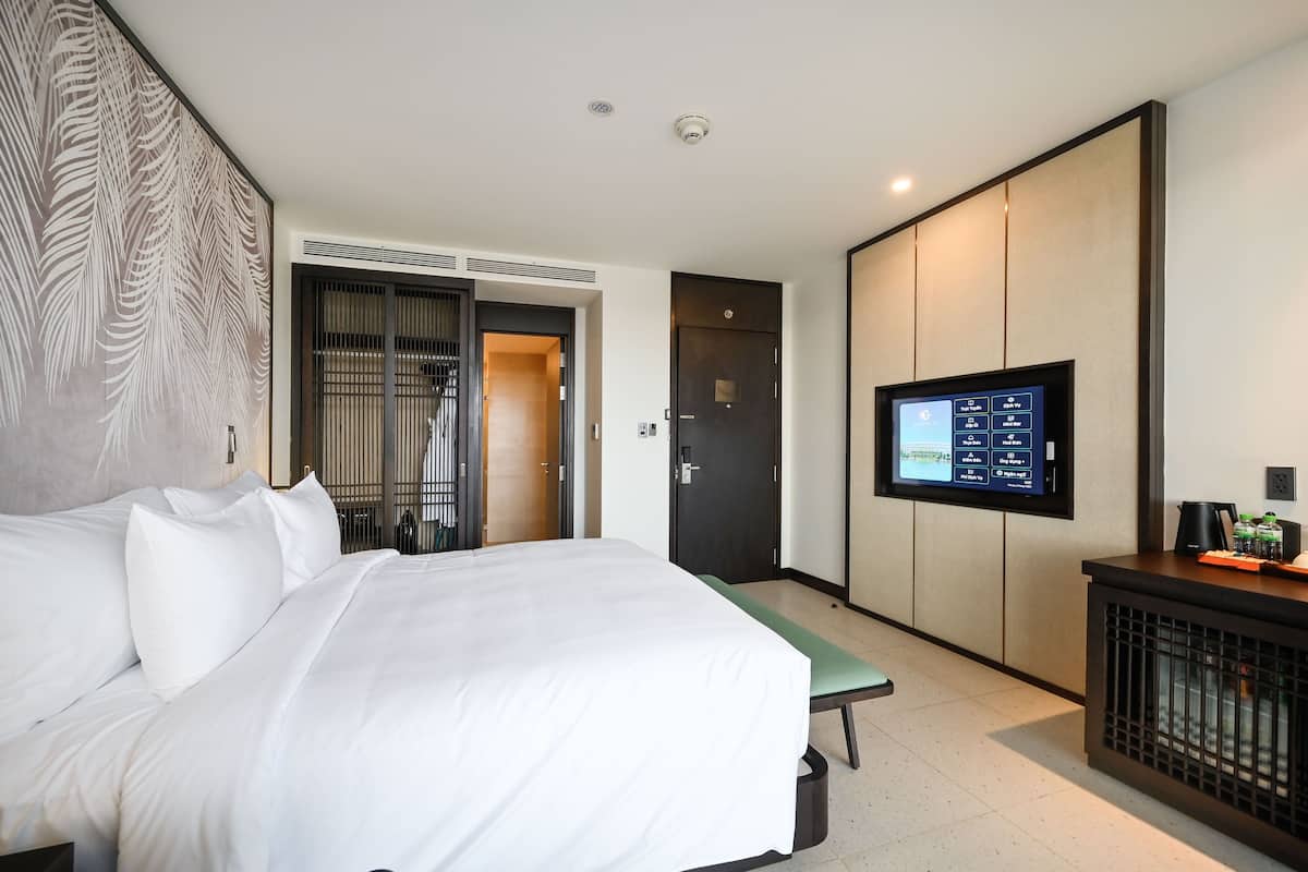 A hotel room with a large bed, a TV mounted on the wall, a desk with a coffee maker, and a sliding door leading to a bathroom.