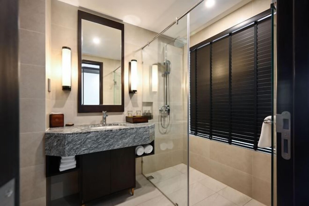 A modern bathroom with a marble sink, a large mirror, a glass-enclosed shower, and a dark sliding door.
