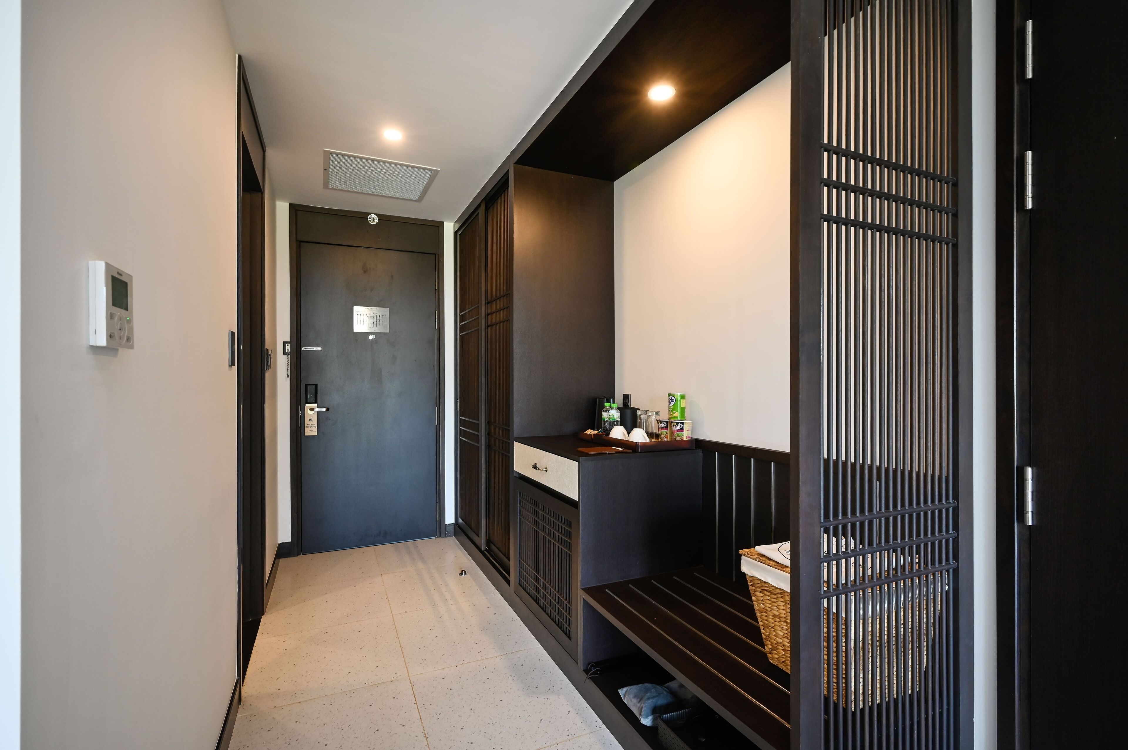 A hallway with a dark door, a thermostat, and a small counter with items on it.