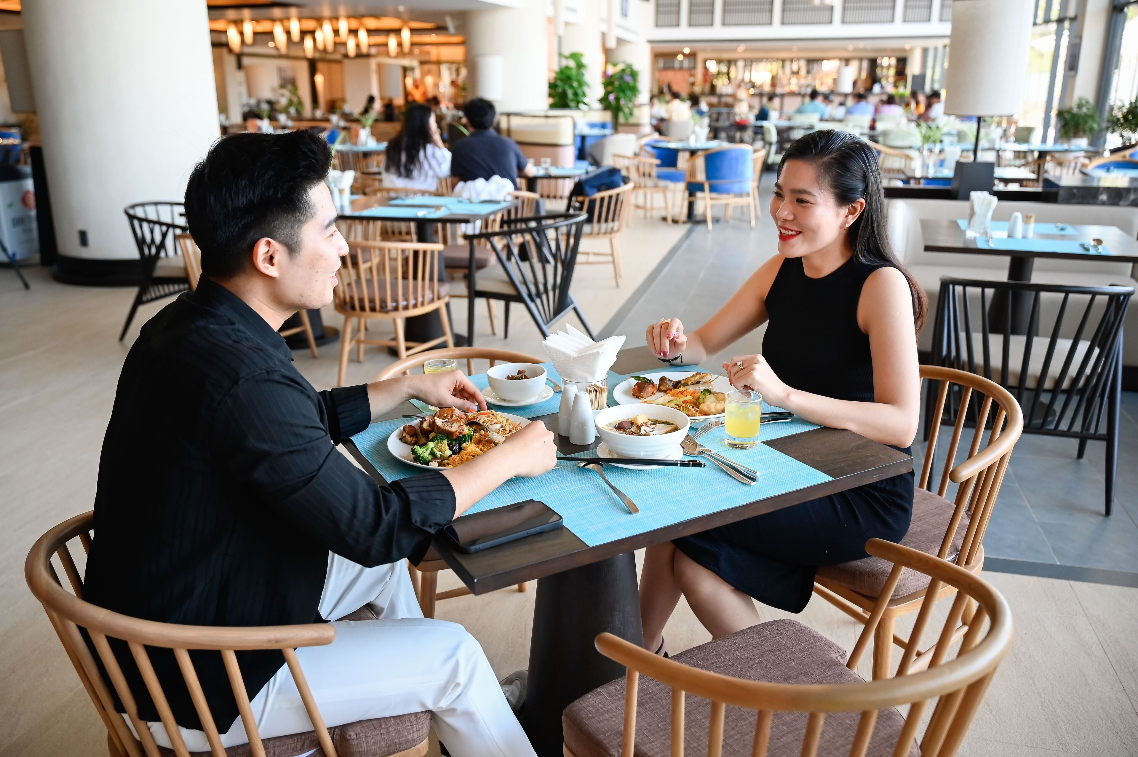 A couple dining at a restaurant with a view of other diners and a modern interior.