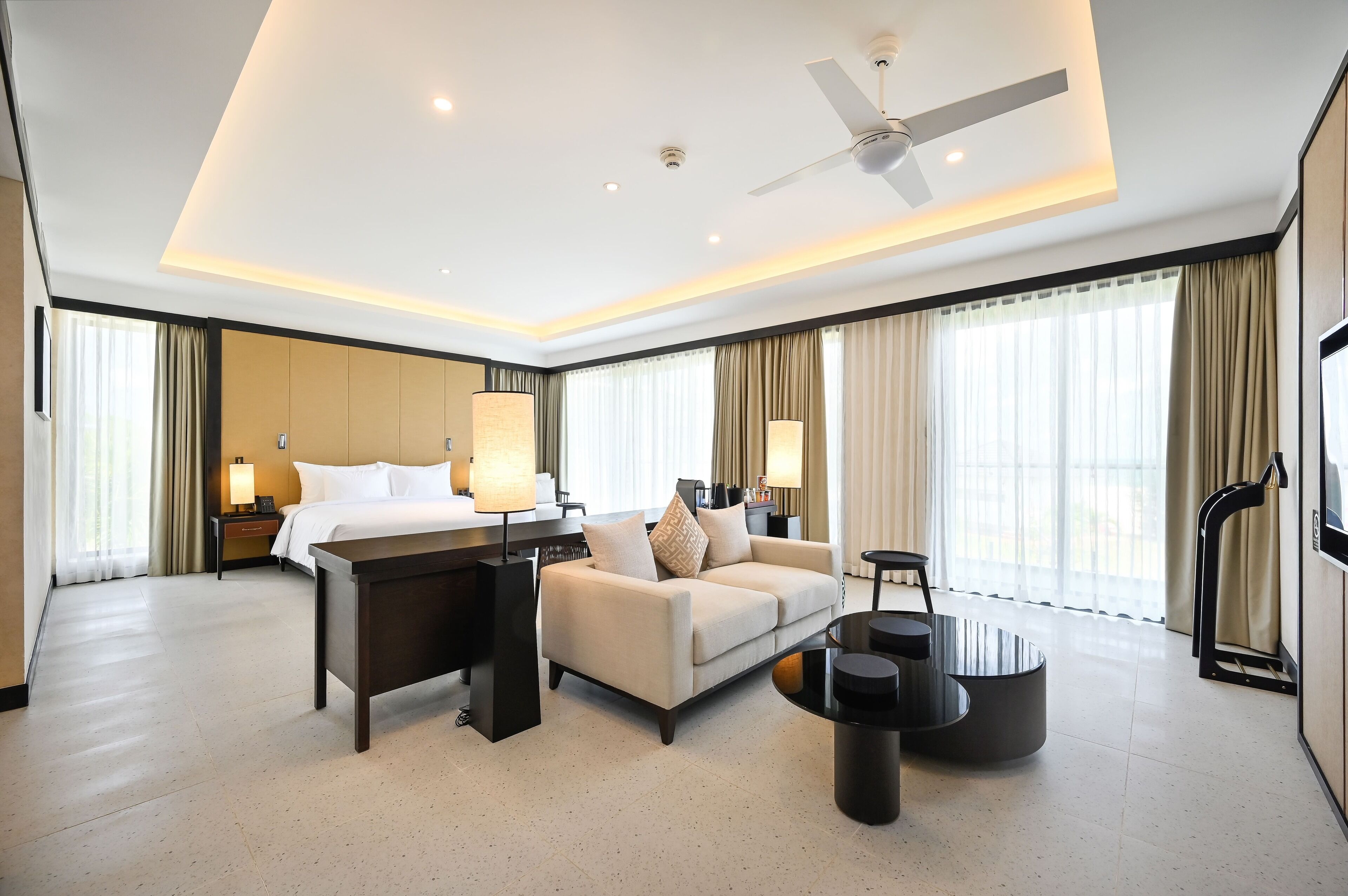 Quarto de hotel moderno com cama, sofá, mesa de centro e escrivaninha com luminária.