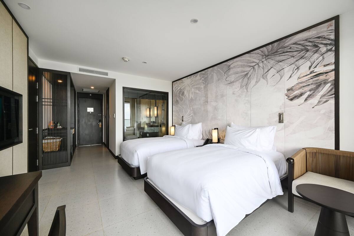 A hotel room with two beds, a large wall art piece, a seating area, and a view into the hallway.