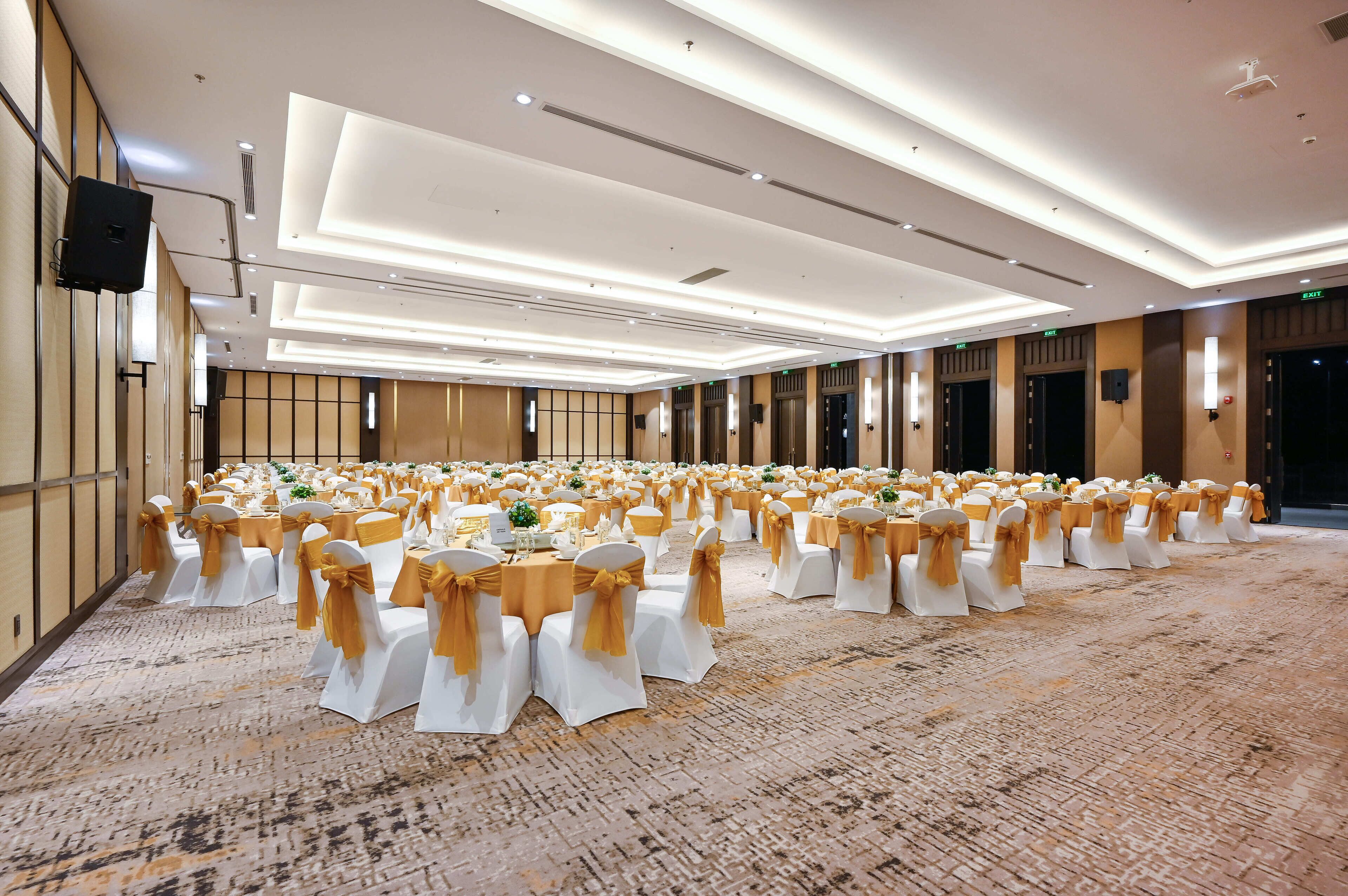 A large banquet hall with rows of tables and chairs, each with white tablecloths and gold sashes.