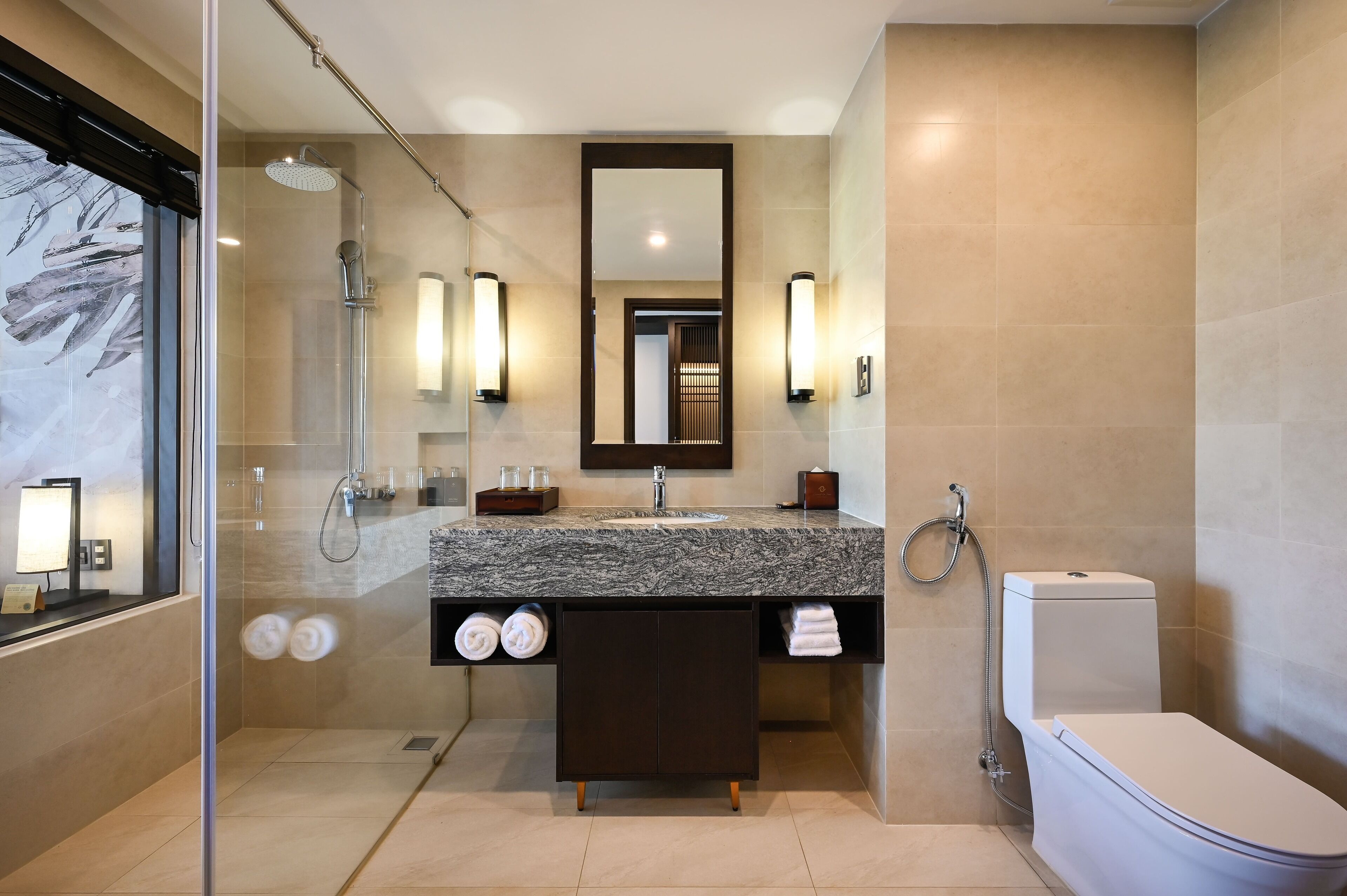 Un baño moderno con ducha envuelta en vidrio, lavamanos de mármol, un espejo grande y un inodoro.