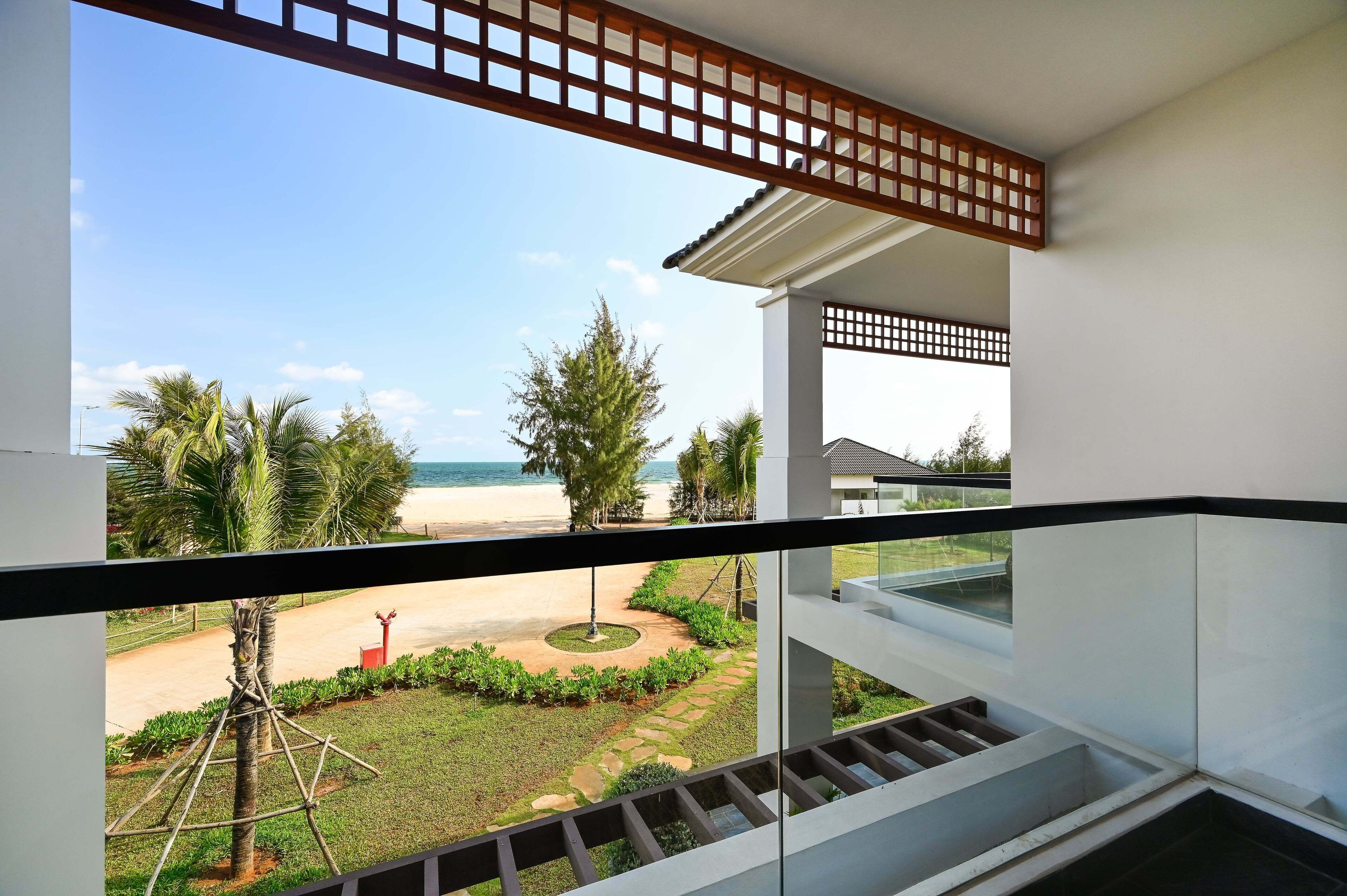 A balcony with a view of a beach, palm trees, and a clear sky.