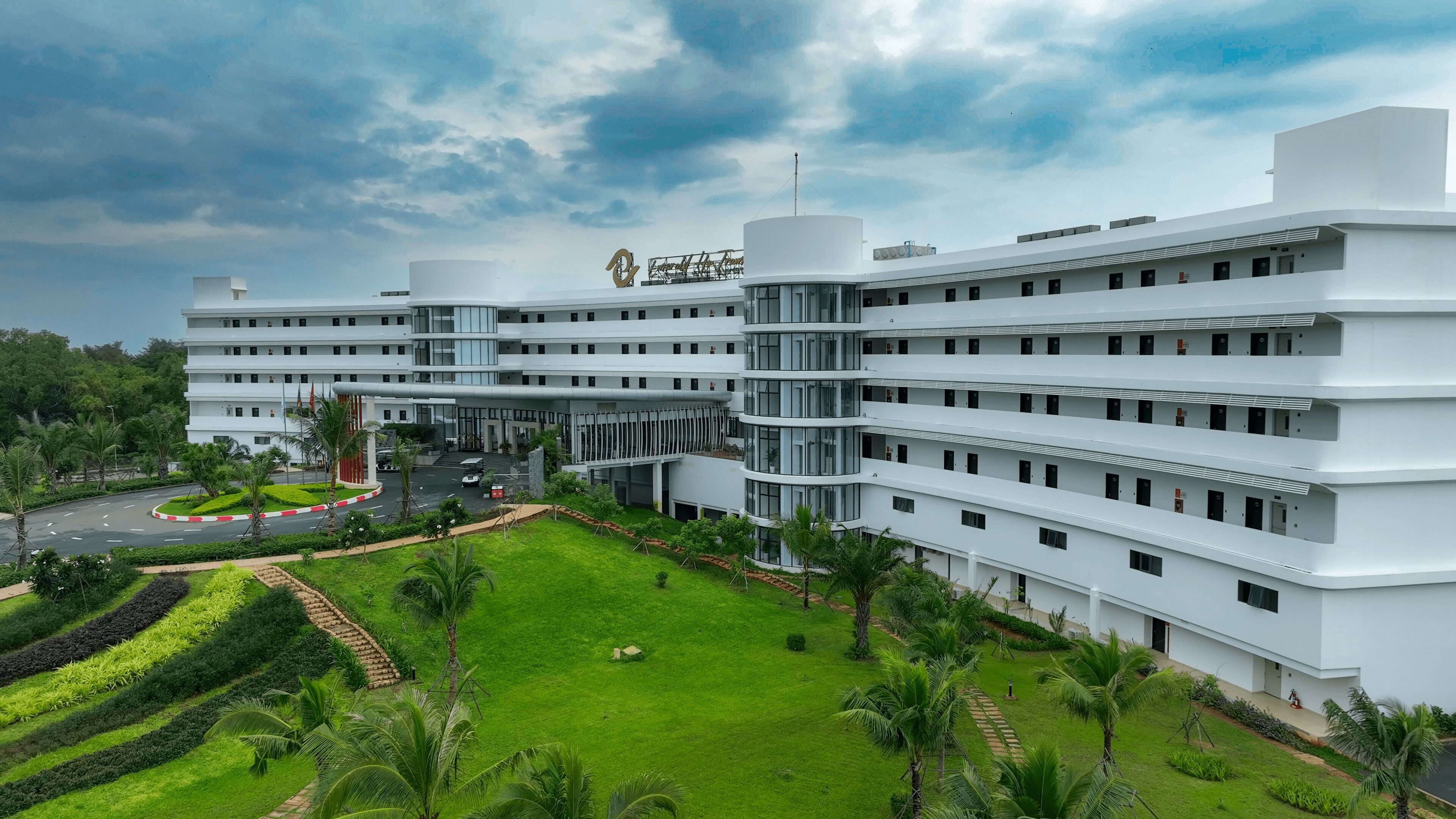 A modern multi-story building with a central courtyard, surrounded by lush greenery and palm trees.