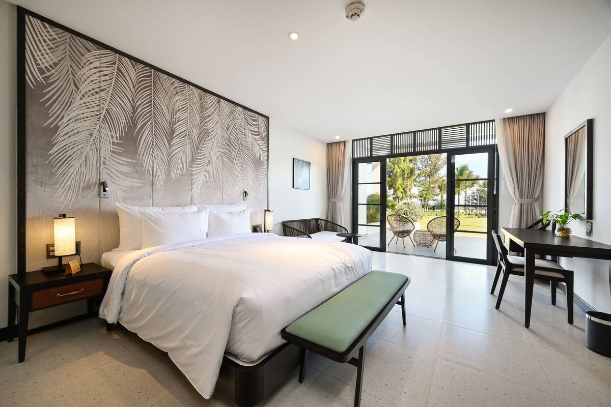 A modern hotel room with a large bed, a desk, and a balcony with a view.